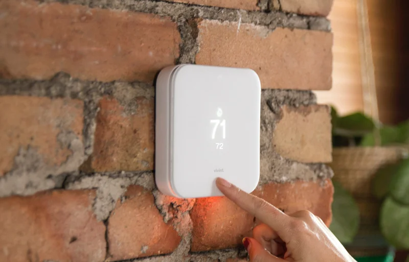 A person pointing at a thermostat on a brick wall.